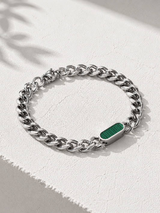 A silver-toned curb chain bracelet with a polished rectangular green inlay, displayed on a textured white surface with soft leaf shadows.
