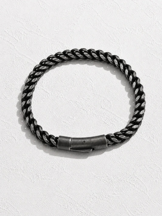 A thick braided rope-style bracelet in black and silver tones with a dark metal clasp, displayed on a textured white background.