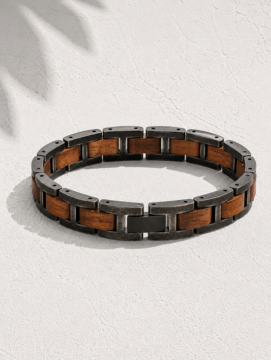 A circular link bracelet featuring alternating dark metallic and warm brown wood links, displayed on a textured off-white surface with soft leaf shadows.